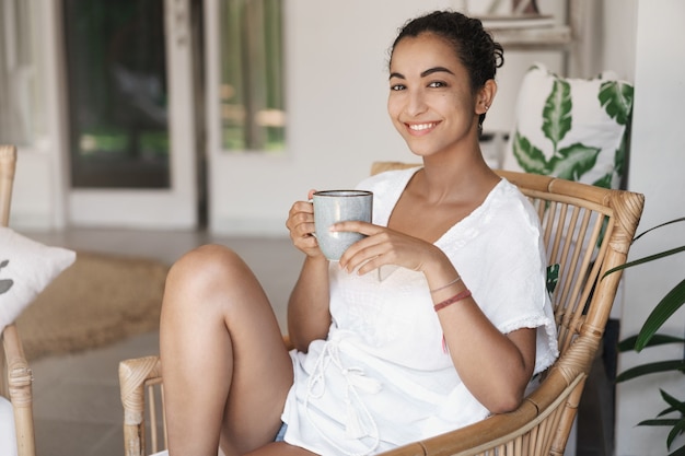 Inschrijving ontspannen vrouw genieten van kopje koffie zittend op rotan fauteuil.