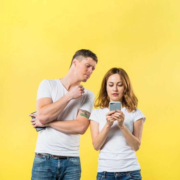 Jaloerse vriend die zijn meisje spioneren lettend op haar telefoon tegen gele achtergrond