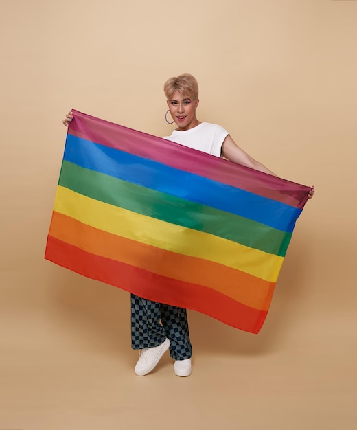 Gratis foto jeugd aziatische transgender lgbt weergegeven: regenboogvlag geïsoleerd over naakt kleur achtergrond