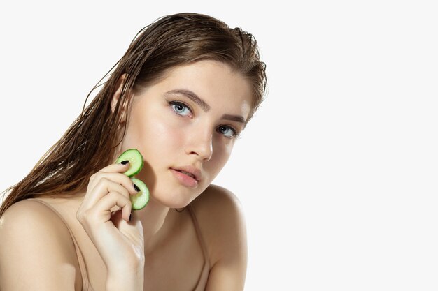Jeugdgeheimen. Close up van mooie jonge vrouw met komkommer op witte achtergrond.