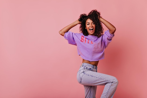 Jocund jonge dame tijd doorbrengen in studio Indoor foto van positieve slanke vrouw met zwart krullend haar