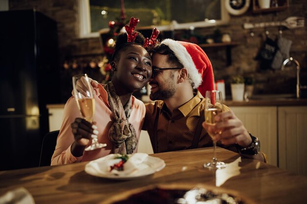 Jong aanhankelijk paar champagne drinken aan eettafel op kerstavond