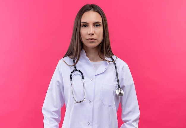 jong artsenmeisje dat stethoscoop medische toga draagt op geïsoleerde roze muur