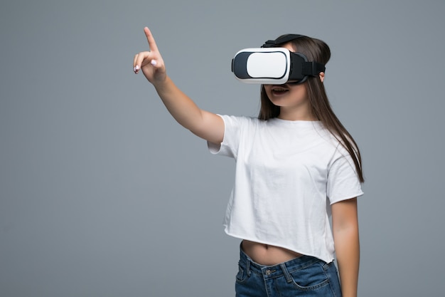 Jong Aziatisch meisje die niettemin VR letten en handaanraking op lucht op grijze achtergrond