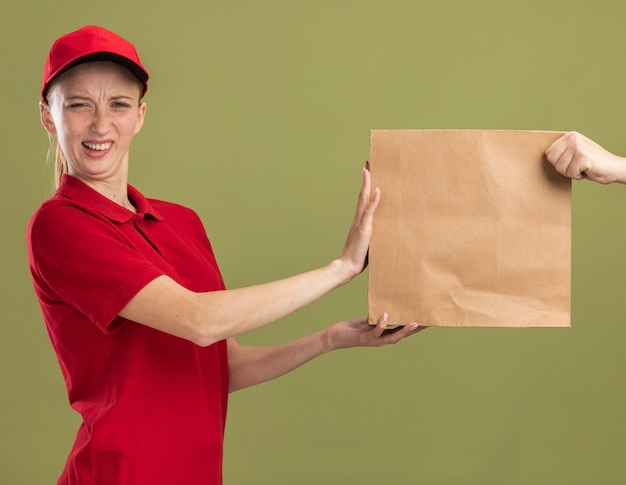 Jong bezorgmeisje in rood uniform en pet weigert papieren pakket te ontvangen