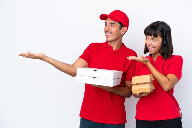 Jong bezorgpaar met pizza's en hamburgers geïsoleerd op een witte achtergrond, terugwijzend en een product presenterend
