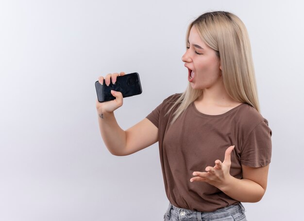 Jong blondemeisje zingen gebruikend telefoon als microfoon op geïsoleerde witte muur met exemplaarruimte