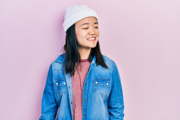 Gratis foto jong chinees meisje met een schattige wollen muts die wegkijkt naar de zijkant met een glimlach op de natuurlijke uitdrukking van het gezicht zelfverzekerd lachend