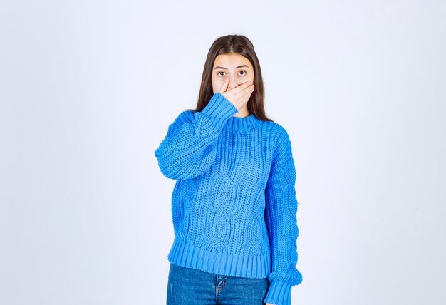 Jong donkerbruin meisje in blauwe sweater die haar mond op wit kegelen.