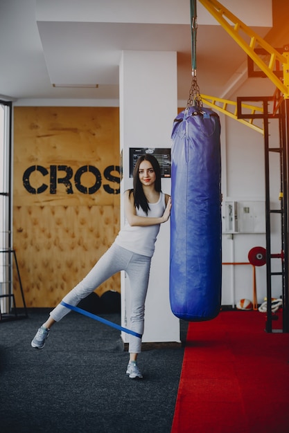 jong en mager meisje in een wit shirt en grijze beenkappen die zich bezighouden met sporten in de sportschool