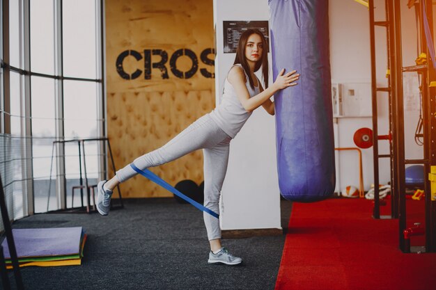 jong en mager meisje in een wit shirt en grijze beenkappen die zich bezighouden met sporten in de sportschool