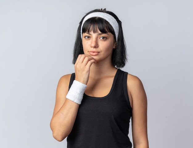 Gratis foto jong fitnessmeisje dat een hoofdband draagt en naar de camera kijkt, verbaasd staat over een witte achtergrond