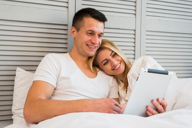 Jong gelukkig paar met tablet onder deken op bed