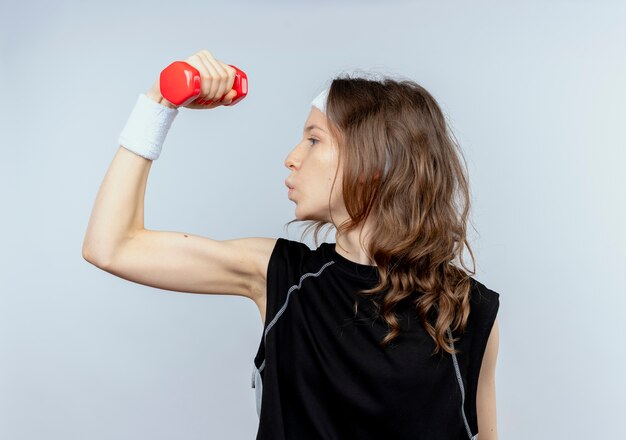 Jong geschiktheidsmeisje in zwarte sportkleding met hoofdband die met domoor uitwerken die zelfverzekerd over witte muur kijken