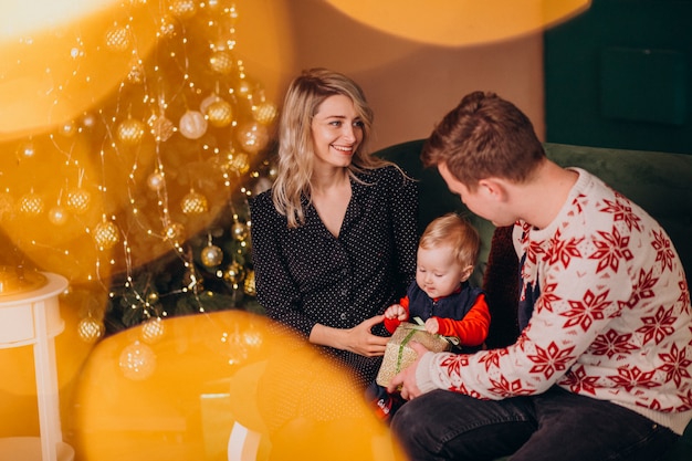 Jong gezin met baby meisje zitten door kerstboom