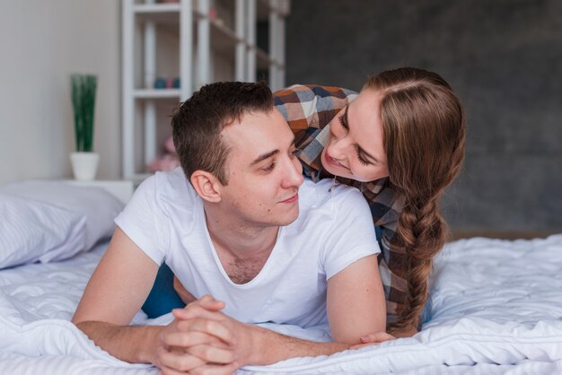 Jong glimlachend paar die en op bed thuis koesteren liggen