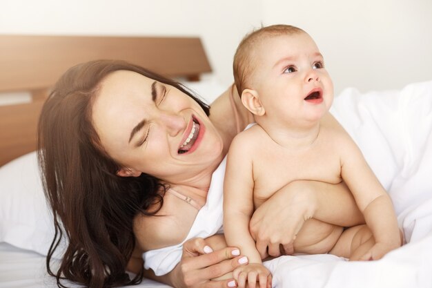 Jong grappig mamma die de aap spelen haar baby schreeuwen die thuis in bed liggen.