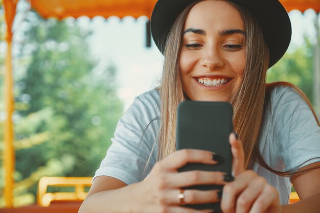 Jong hipstermeisje in trendy smartphone van de hoedenholding in handen