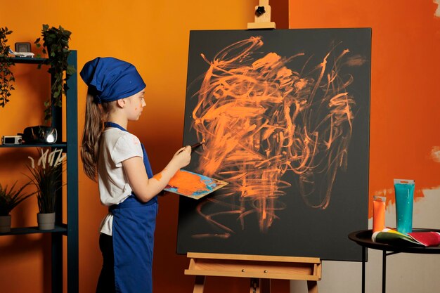 Jong kind met oranje verfkleur op canvas, kunstwerk meesterwerk makend met colormix lade en aquarelle palet. Schilderinspiratieontwerp met penseel, waterverf en vaardigheden.