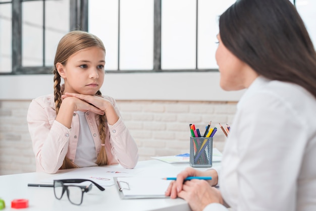 Jong kinderpsycholoog die met droevig meisje in het bureau spreekt