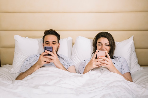 Jong koppel in bed met behulp van smartphones