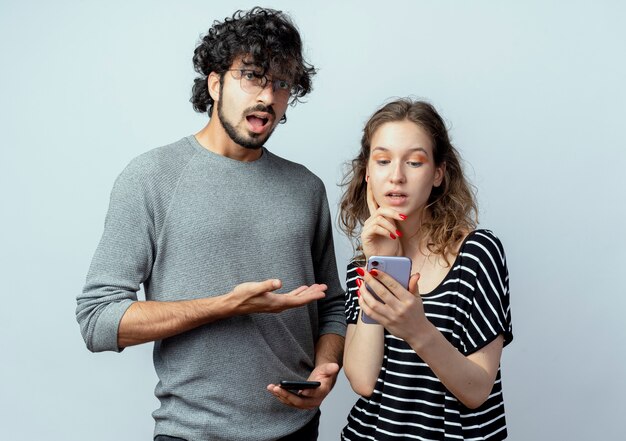 Jong koppel man en vrouw, boos man wijzend op zijn vriendin die smartphone staande houden op witte achtergrond