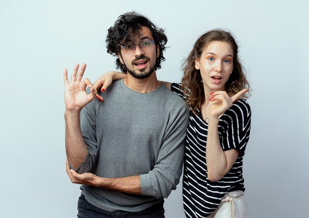 jong koppel man en vrouw lachend gelukkig en positief man weergegeven: ok teken staande over witte muur