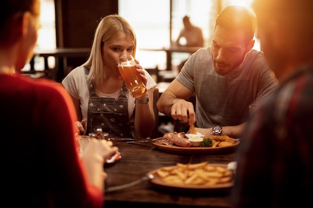 Jong koppel samenkomen met vrienden in een pub en genieten van bier en eten