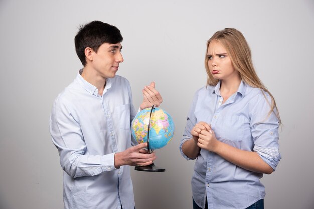 Jong koppel staande met een Earth globe op grijze muur