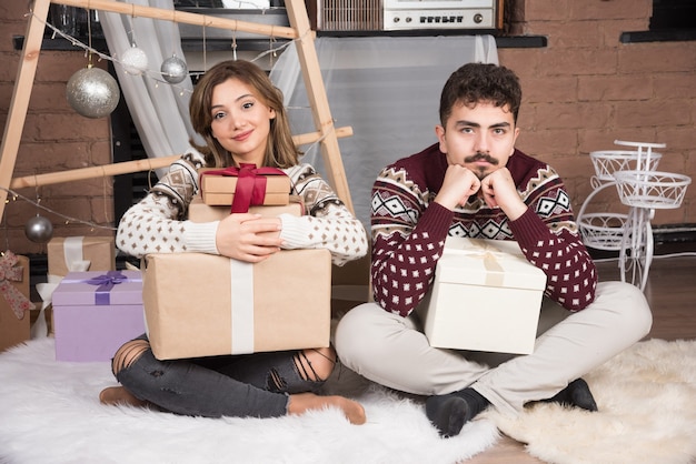 Jong koppel zit met kerstcadeautjes in de buurt van feestelijke zilveren ballen.