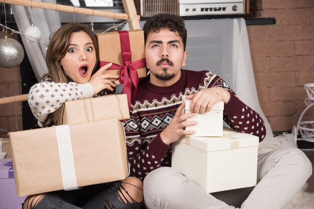 Jong koppel zit met kerstcadeautjes in de buurt van feestelijke zilveren ballen.