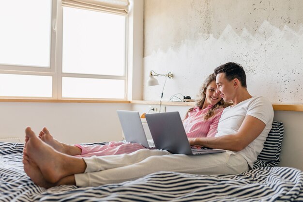Jong koppel zittend op bed in de ochtend, man en vrouw die op laptop werkt