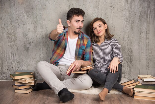 Jong koppel zittend op de vloer met boeken en duimen opgevend