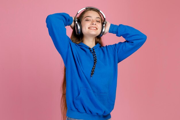 Jong lachend meisje gooit handen achter het hoofd terwijl ze binnenshuis geniet van haar favoriete liedje met oortelefoons