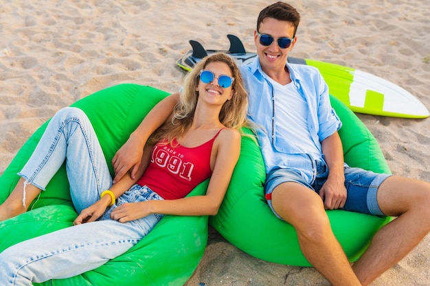 Gratis foto jong lachend paar plezier op het strand zittend op zand met surfplanken