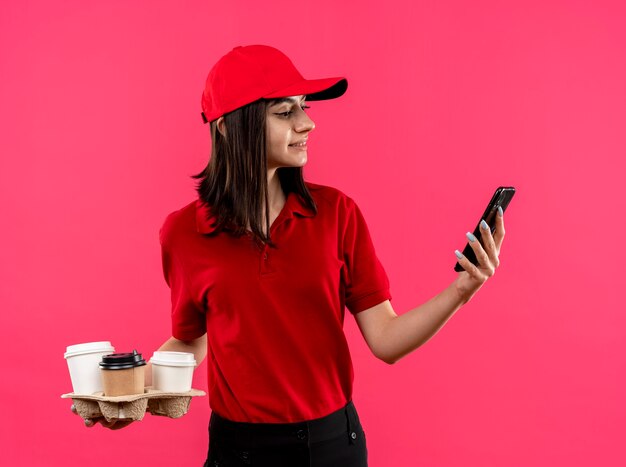 Jong leveringsmeisje die rood poloshirt en GLB dragen die voedsel packagestanding over roze muur houden