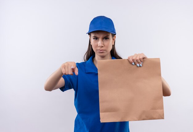 Jong leveringsmeisje in blauw uniform en GLB die document pakket houden die met vinger naar camera met boos fronsend gezicht richten