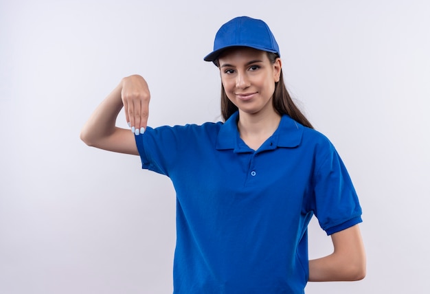 Jong leveringsmeisje in blauw uniform en pet die zelfverzekerd gebaren met handen, lichaamstaalconcept kijken