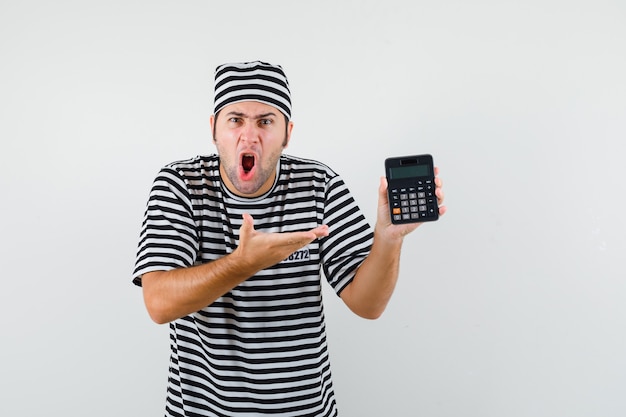 Jong mannetje dat calculator in t-shirt, hoed toont en agressief, vooraanzicht kijkt.