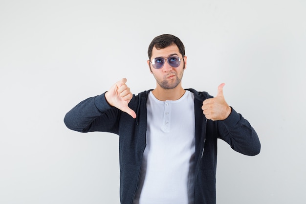 Jong mannetje dat duimen op en neer in t-shirt, jasje toont en aarzelend kijkt. vooraanzicht.