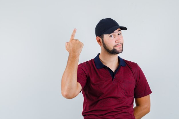 Jong mannetje dat één ideegebaar in rood t-shirt, zwarte pet toont en gericht kijkt. vooraanzicht.