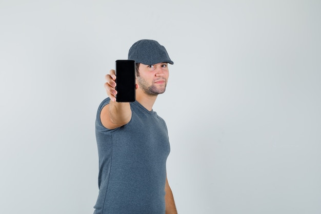 Jong mannetje dat mobiele telefoon in t-shirtglb toont en zelfverzekerd kijkt