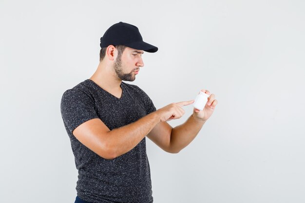 Jong mannetje dat op info over fles pillen in t-shirt en GLB richt en voorzichtig kijkt