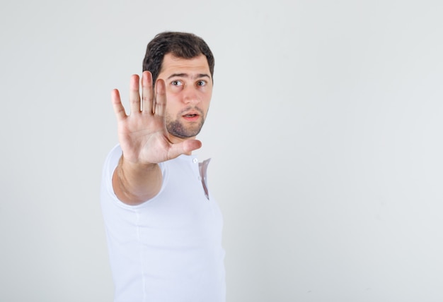 Jong mannetje dat stopgebaar in wit t-shirt toont en walgt kijkt