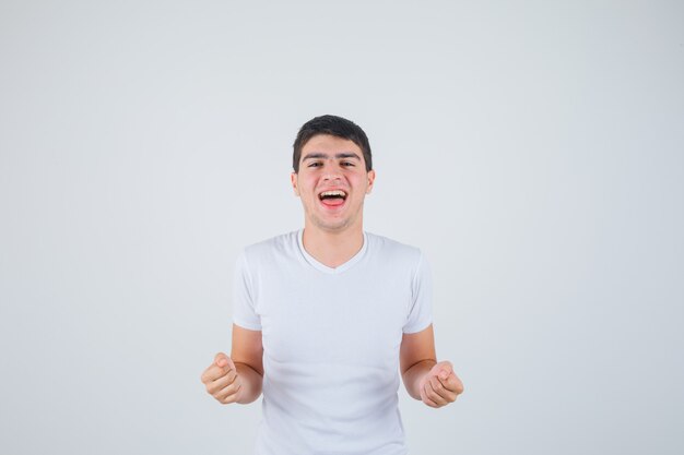 Jong mannetje dat winnaargebaar in t-shirt toont en gelukkig kijkt. vooraanzicht.