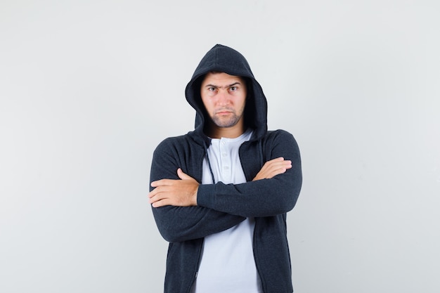 Jong mannetje dat zich met gekruiste wapens in t-shirt, jasje bevindt en ernstig, vooraanzicht kijkt.