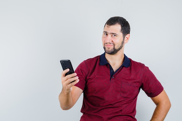 Jong mannetje in de rode telefoon van de t-shirtholding en klaar, vooraanzicht kijkt.