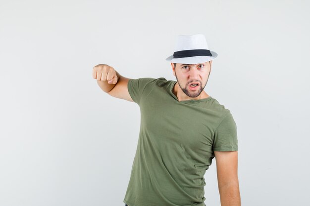 Jong mannetje in groen t-shirt en hoed die met vuist bedreigen en zenuwachtig kijken