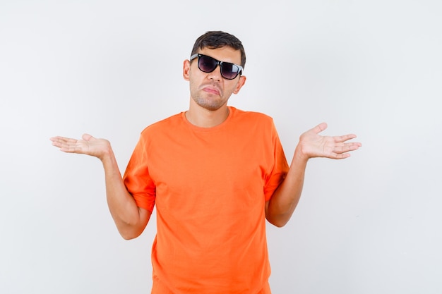 Jong mannetje in oranje t-shirt die hulpeloos gebaar toont en verward kijkt
