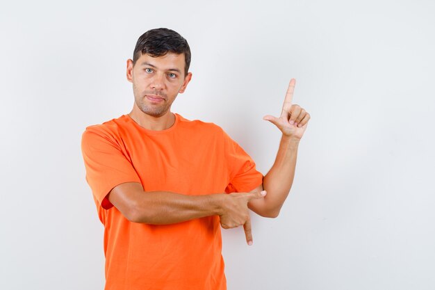 Jong mannetje in oranje t-shirt die op en neer wijst en verstandig kijkt